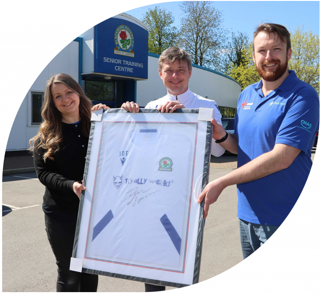A photo of 3 people smiling with one holding a signed sports shirt in a frame.